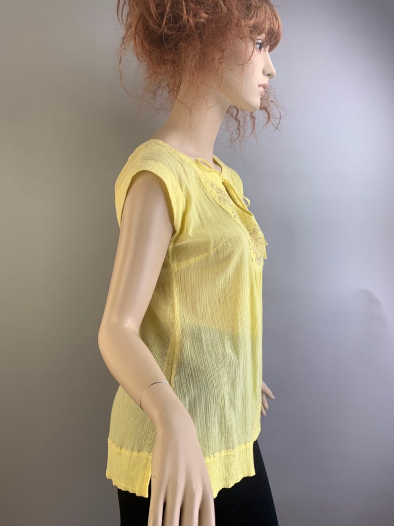 May include: A yellow sheer blouse with a tie at the neckline and embroidered details.