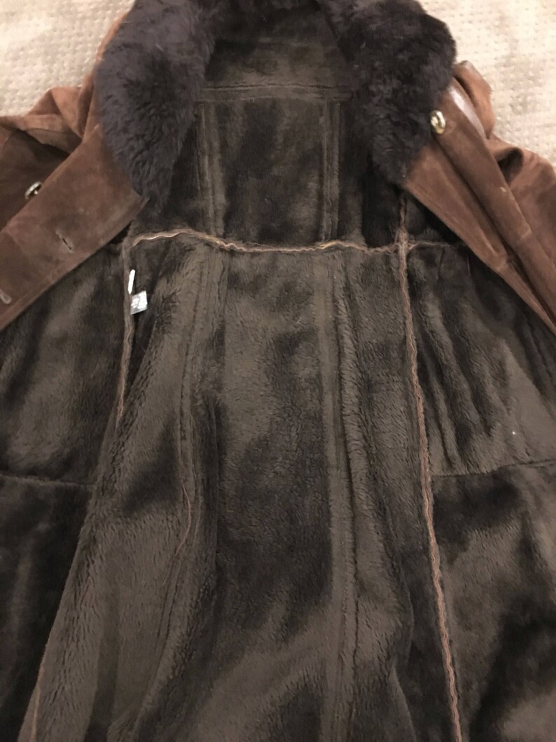 May include: A brown suede coat with a dark brown fur collar and lining. The coat features a button closure and a classic design, ideal for cold weather. The interior is a plush, dark brown material.