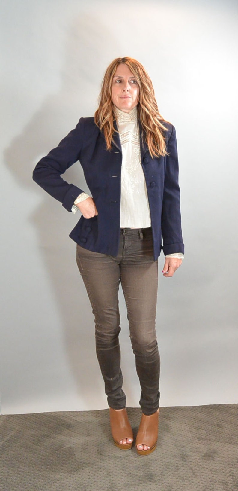 May include: A woman wearing a navy blue blazer over a white lace blouse, brown jeans, and brown open-toe heeled shoes.
