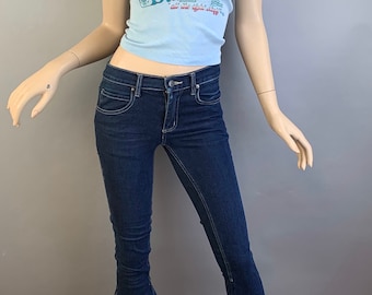 May include: A blue tank top with a Harley Davidson logo and a red rose graphic. The tank top is paired with dark blue bell bottom jeans.