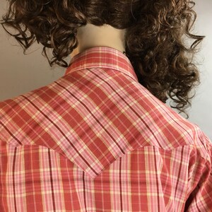 May include: A red and pink plaid shirt with a yoke in the back. The shirt is made of a soft, lightweight fabric and has a classic button-down collar.