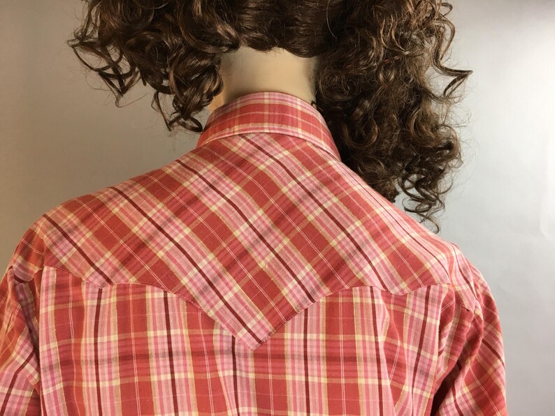 May include: A red and pink plaid shirt with a yoke in the back. The shirt is made of a soft, lightweight fabric and has a classic button-down collar.