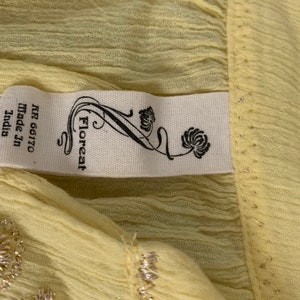 May include: A pale yellow fabric with a white tag that reads "Floreat" and "NR 66170 Made in India". The fabric has a subtle shimmer and a delicate texture.