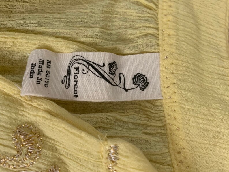 May include: A pale yellow fabric with a white tag that reads "Floreat" and "NR 66170 Made in India". The fabric has a subtle shimmer and a delicate texture.