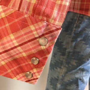 May include: Close-up of a red and yellow plaid shirt cuff with three silver snaps.