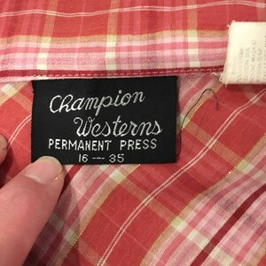 May include: A red and white plaid shirt with a black label that reads "Champion Westerns Permanent Press 16 - 35".