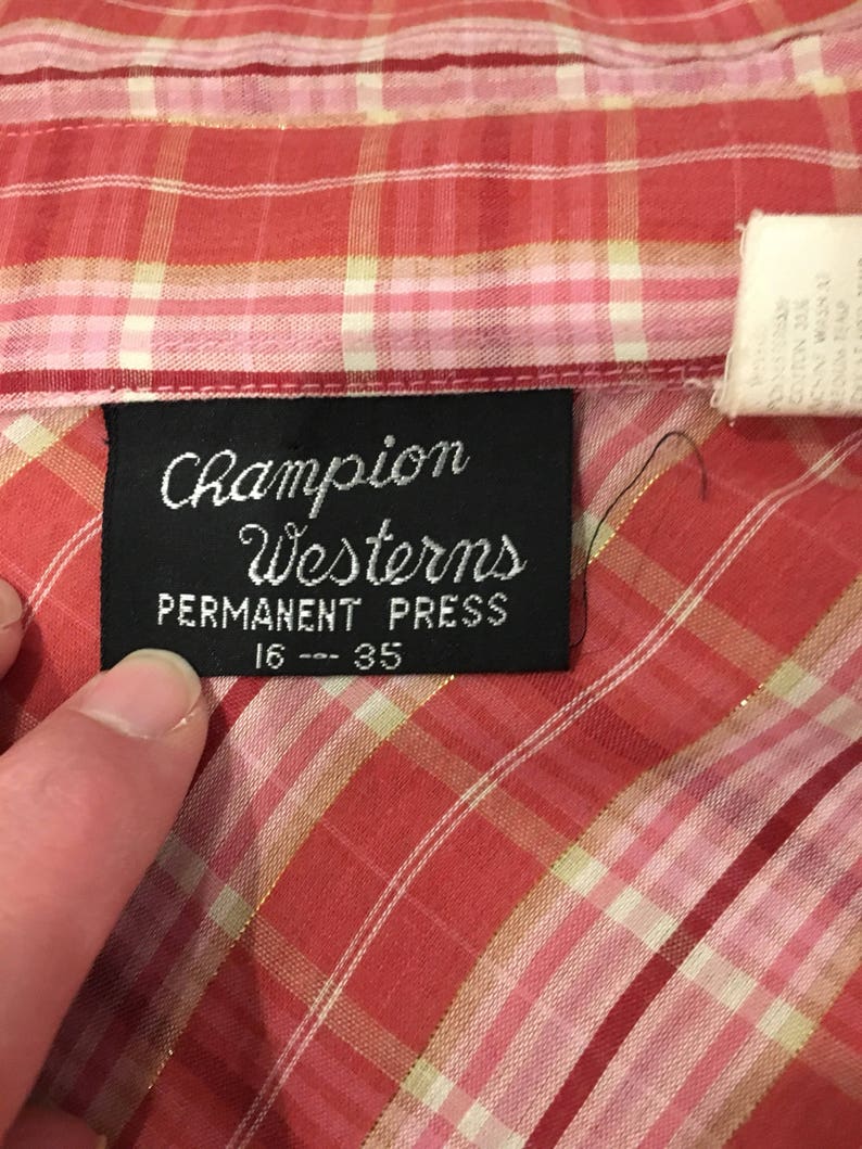 May include: A red and white plaid shirt with a black label that reads "Champion Westerns Permanent Press 16 - 35".