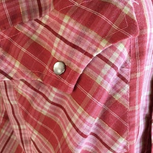 May include: A red and white plaid shirt with a single silver button on the pocket.