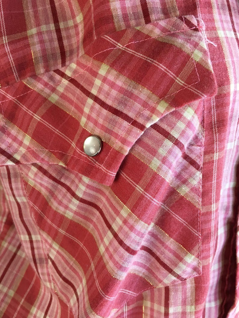May include: A red and white plaid shirt with a single silver button on the pocket.