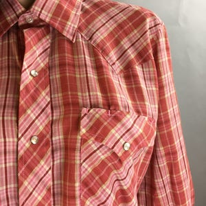 May include: A red and pink plaid long-sleeve shirt with a button-down collar and two chest pockets.