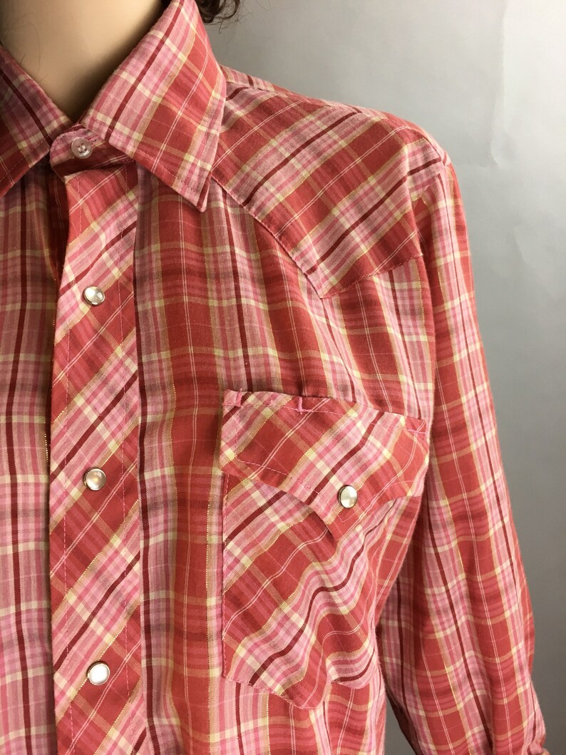 May include: A red and pink plaid long-sleeve shirt with a button-down collar and two chest pockets.