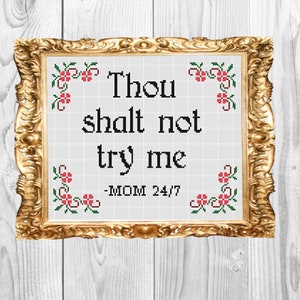 Op de afbeelding: Een ingelijst kruissteek met de tekst "Thou shalt not try me - MOM 24/7" omringd door een bloemmotief.