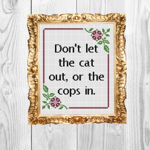 Puede incluir: Un bordado de punto de cruz enmarcado con un marco dorado y un fondo blanco. El bordado presenta el texto "Don't let the cat out, or the cops in." con dos flores rosas a cada lado del texto.