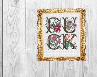 May include: Cross-stitch artwork in a gold ornate frame. The word "FUCK" is spelled out in dark brown letters, each filled with colorful flowers. The background is a white wooden surface.