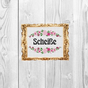 Puede incluir: Un bordado de punto de cruz enmarcado en oro con flores rosas y verdes que rodean la palabra "Scheiße".