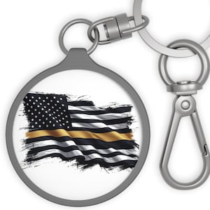 May include: A circular silver-toned keyring featuring a graphic of a waving American flag with a single horizontal gold stripe across the black and white field. The keyring includes a round split ring and a swivel lobster clasp attachment.
