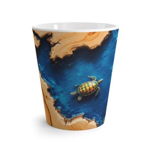 Könnte beinhalten: Eine weiße Latte-Tasse aus Keramik mit einem Design einer Meeresschildkröte, die in blauem Wasser schwimmt. Die Außenseite der Tasse hat eine holzähnliche Textur an den Seiten, die einen Kontrast zur Ozeanszene bildet. Die Tasse ist etwa 13 cm hoch.
