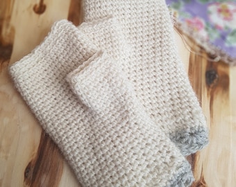 Può includere: Due scaldapolsi lavorati all'uncinetto a mano, di colore crema chiaro, con bordo smerlato grigio. I scaldapolsi sono realizzati con un filato spesso e sono esposti su una superficie di legno. La maglia all'uncinetto crea un aspetto strutturato.