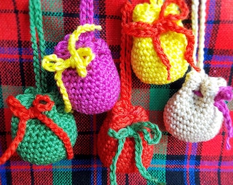 May include: Five crocheted drawstring bags in different colors, including green, red, pink, yellow, and beige, hanging on a red and green plaid fabric.