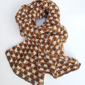 Puede incluir: Una bufanda de punto a cuadros marrones y blancos. La bufanda está hecha de un hilo suave y cálido, perfecta para mantenerte abrigado en invierno.