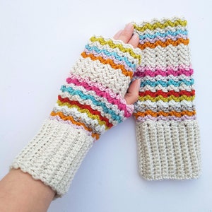 May include: Hand-crocheted fingerless gloves in cream with colorful horizontal stripes in shades of pink, orange, yellow, and blue. The gloves have a ribbed cuff and a zig-zag pattern on the upper part.