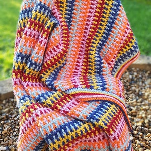 May include: A colorful crocheted blanket with stripes of pink, orange, yellow, red, blue, and gray. The blanket is draped over a chair.