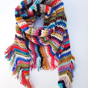 Peut inclure: Une écharpe en crochet colorée avec des franges. L'écharpe est faite avec une variété de couleurs, y compris le rouge, le bleu, le vert, le jaune et le violet.