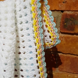 May include: White crochet blanket with a colourful border of yellow, pink and blue yarn.