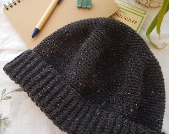 May include: A dark gray beanie with a flecked texture. The beanie is made of a soft, knitted fabric.