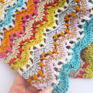 May include: A colourful crocheted blanket with a scalloped edge and gold thread accents.