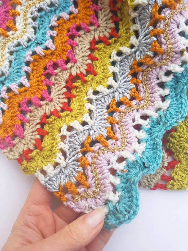 May include: A colourful crocheted blanket with a scalloped edge and gold thread accents.