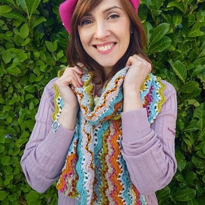 May include: A woman wearing a pink beret with white trim and a colourful crocheted scarf. The scarf has a variety of colours, including blue, green, orange, and pink.