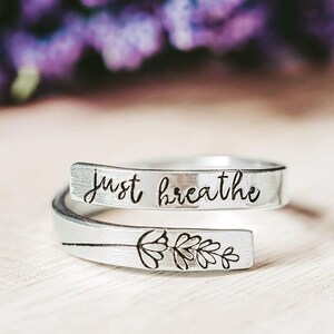 May include: Two silver rings with a delicate floral design and the words "Just Breathe" engraved on one of the rings.