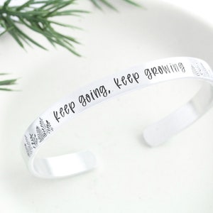 May include: Silver bracelet with the inscription "keep going. keep growing." and a design of small trees on the side.