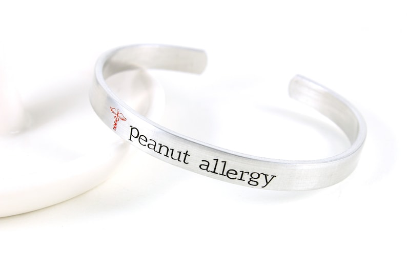 May include: Silver bracelet with the text "peanut allergy" and a red medical symbol.