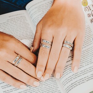 May include: Close-up of a person's hands wearing three silver rings with engraved messages. The rings say "one day at a time", "till we meet again", and "grit & grace".