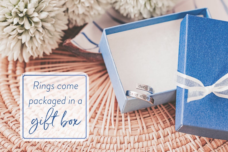 May include: A blue gift box tied with a white ribbon, containing two silver rings. The rings are engraved with the words "don't let" and "hard days". The image also includes text that reads "Rings come packaged in a gift box".