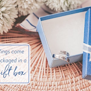 May include: Two silver rings in a blue gift box with a white ribbon. The rings are engraved with the words "don't let the hard days win". Rings come packaged in a gift box.