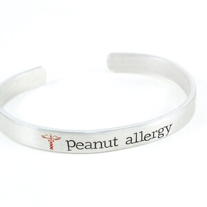 May include: Silver bracelet with the text "Peanut allergy" and a red medical symbol.