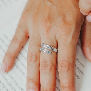 May include: A silver ring with the words "Inhale, exhale" engraved on it. The ring is worn on a person's finger.