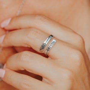 May include: A silver ring with a delicate floral design. The ring is open and wraps around the finger.