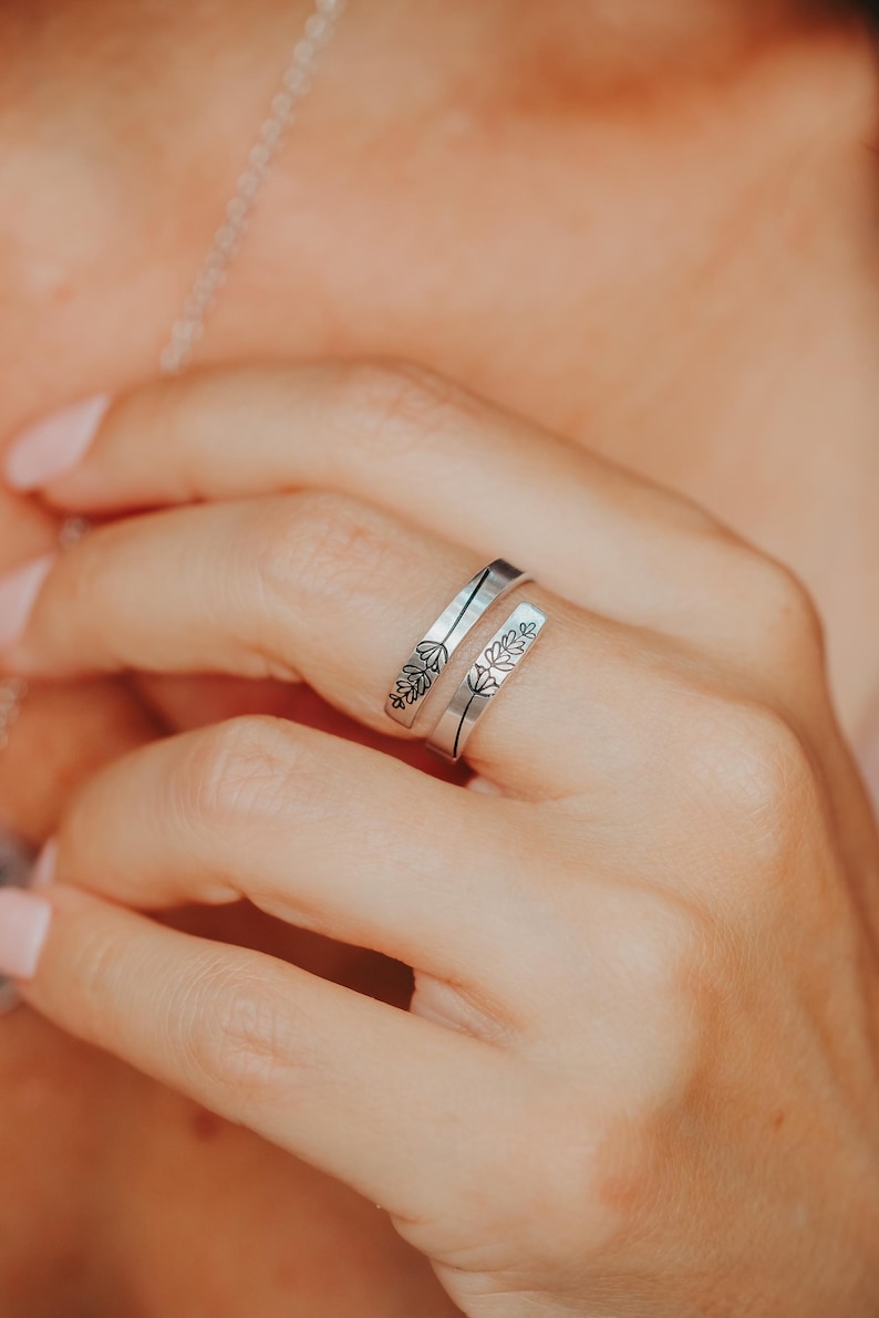 May include: A silver ring with a delicate floral design. The ring is open and wraps around the finger.