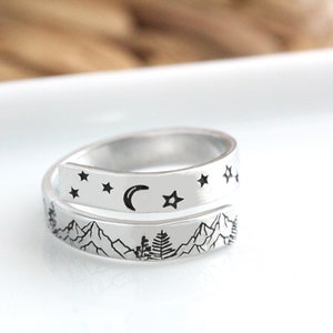 May include: A silver ring with a design of mountains, a crescent moon, and stars. The ring is open and can be adjusted to fit different finger sizes.