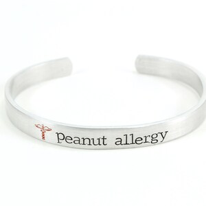 May include: A silver bracelet with the text "Peanut allergy" and a red medical symbol engraved on it.