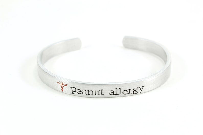 May include: A silver bracelet with the text "Peanut allergy" and a red medical symbol engraved on it.