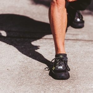 Puede incluir: Primer plano de un pie que lleva zapatos deportivos negros y verdes con cordones blancos. El zapato tiene una suela negra y una parte superior verde y negra.