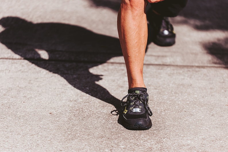 Puede incluir: Primer plano de un pie que lleva zapatos deportivos negros y verdes con cordones blancos. El zapato tiene una suela negra y una parte superior verde y negra.
