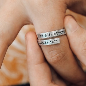 May include: A silver ring engraved with the words "she is strong" and "Proverbs 31:25".