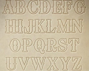 May include: A set of uppercase letters and numbers in a western-style font. The letters are outlined in white and are on a beige background.