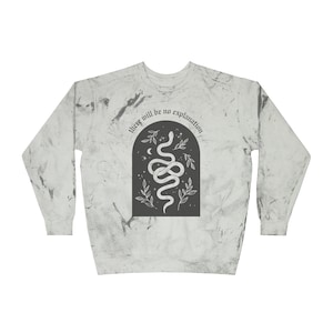 May include: A long-sleeved sweatshirt with a marble-like pattern in shades of gray and white. The front features a dark gray arched design with a white snake, moon, stars, and leaves. The text "there will be no explanation" is above the design.